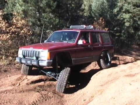 1993 Ford Bronco - This Jeep Cherokee XJ is navigating a steep, sandy incline with one wheel lifted.