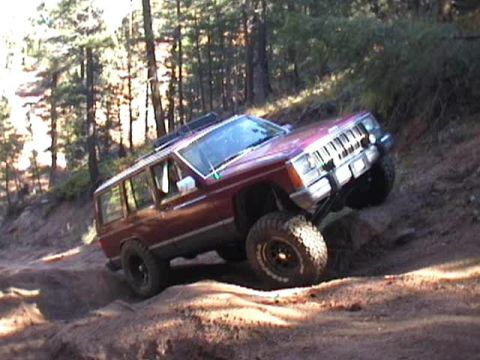 1993 Ford Bronco - This red Jeep Cherokee XJ navigates a steep, sandy incline in a wooded area.
