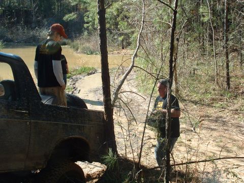 1993 Ford Bronco - Off-road vehicle stuck in the mud with people observing the situation.