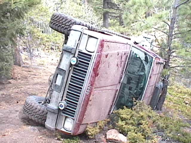 Red Jeep overturned on its side in a wooded area