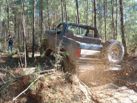 1993 Ford Bronco - Ford Bronco navigates a muddy trail in a wooded area, kicking up dirt.