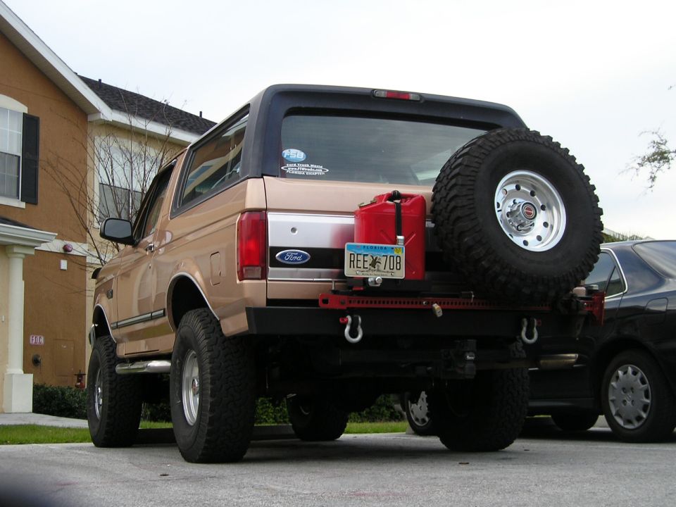 Tan Ford Bronco rear view with spare tire swing-out carrier and gas can in driveway