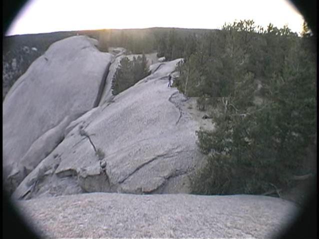 person standing on a large rock formation with trees and a sunset in the background