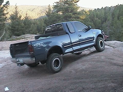 1993 Ford Bronco - A blue pickup truck navigates a rocky terrain with trees in the background.