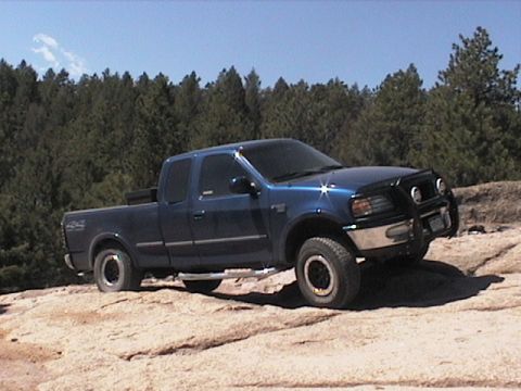 1993 Ford Bronco - Blue Ford F-150 pickup truck with bull bar parked on rocky terrain.