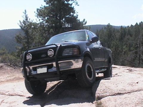 1993 Ford Bronco - A black Ford F-150 navigates rocky terrain with a bull bar on its front end.