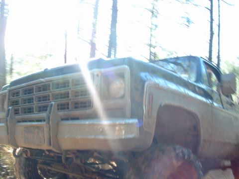1993 Ford Bronco - A muddy truck is seen from the front, driving through a wooded area.