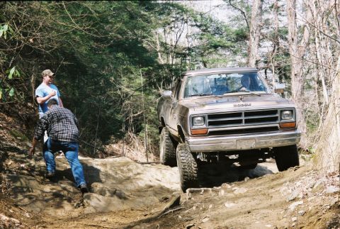 1990 Ford Bronco - A Dodge Ram pickup truck navigates a challenging off-road trail in a wooded area.