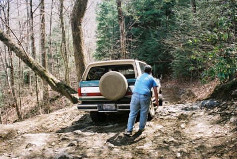 1990 Ford Bronco - A 1990 Ford Bronco navigates a rocky, wooded trail with a person standing behind it.