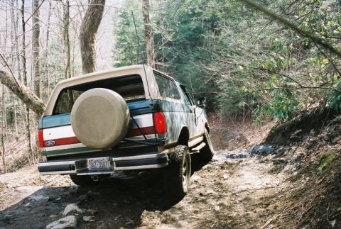 1990 Ford Bronco - Ford Bronco navigates a rough, off-road path through a forest.