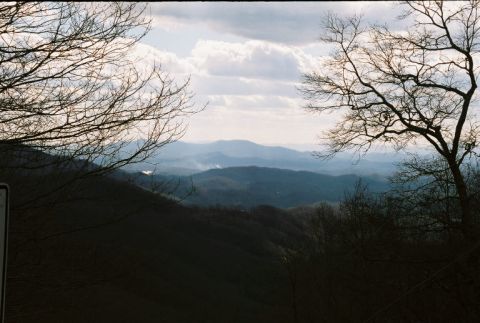1990 Ford Bronco - A scenic view of rolling hills and distant mountains under a cloudy sky, with bare trees framing the shot.