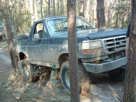 1993 Ford Bronco - This Ford Bronco is navigating a wooded trail, covered in mud from the off-road excursion.