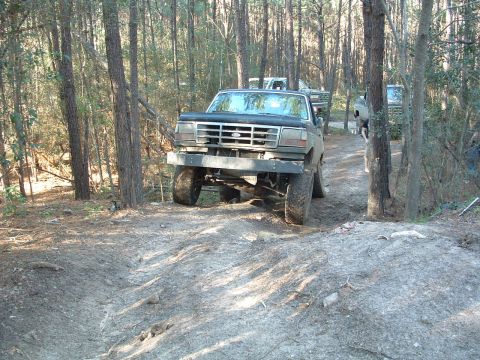 1993 Ford Bronco - A black Ford Bronco navigates a wooded trail with other vehicles in the background.