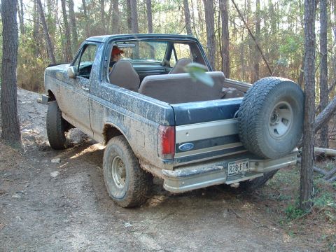 1993 Ford Bronco - Muddy 1993 Ford Bronco navigating a wooded trail with its spare tire visible.