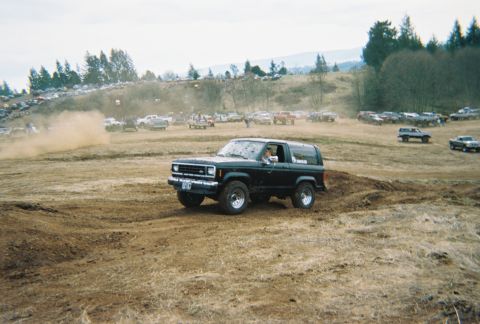 1978 Ford Bronco - A black Ford Bronco II navigates a dirt track during an outdoor event with many other vehicles present.