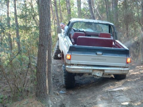 1993 Ford Bronco - Silver and black pickup truck with red interior navigates a wooded trail.