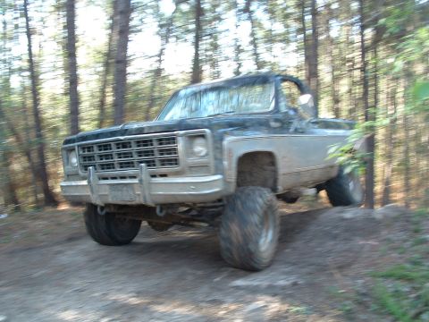 1993 Ford Bronco - This lifted pickup truck is navigating a wooded trail with significant suspension articulation.