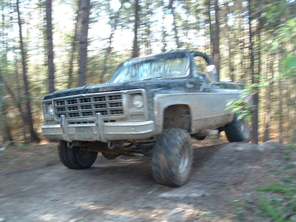 Lifted pickup truck with large tires driving on a dirt path through trees