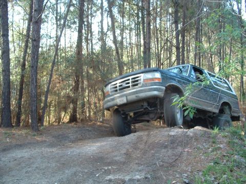 1993 Ford Bronco - A dark green 1992 Ford Bronco navigates a wooded trail, showing its off-road capabilities.