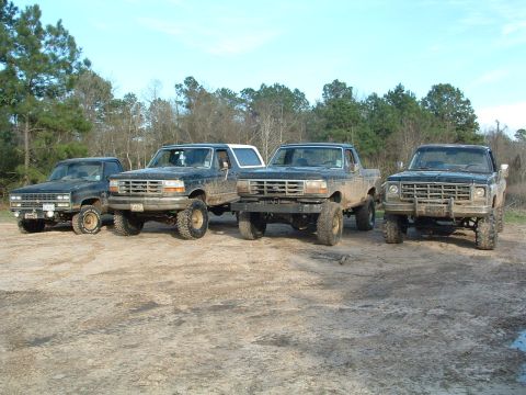 1993 Ford Bronco - Several lifted trucks and a Ford Bronco are parked together on a muddy lot.