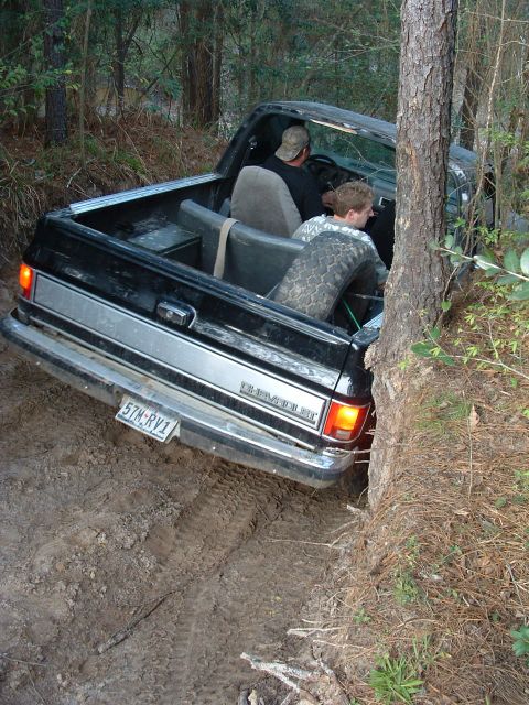 1993 Ford Bronco - A Chevrolet pickup truck is stuck in the mud off-road, with two people inside.