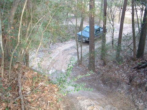 1993 Ford Bronco - A blue SUV navigates a muddy, wooded trail.