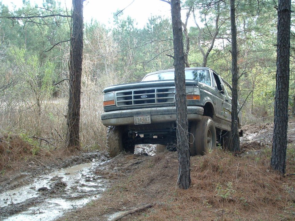 Dark green Ford Bronco on a muddy trail, front 3/4 view