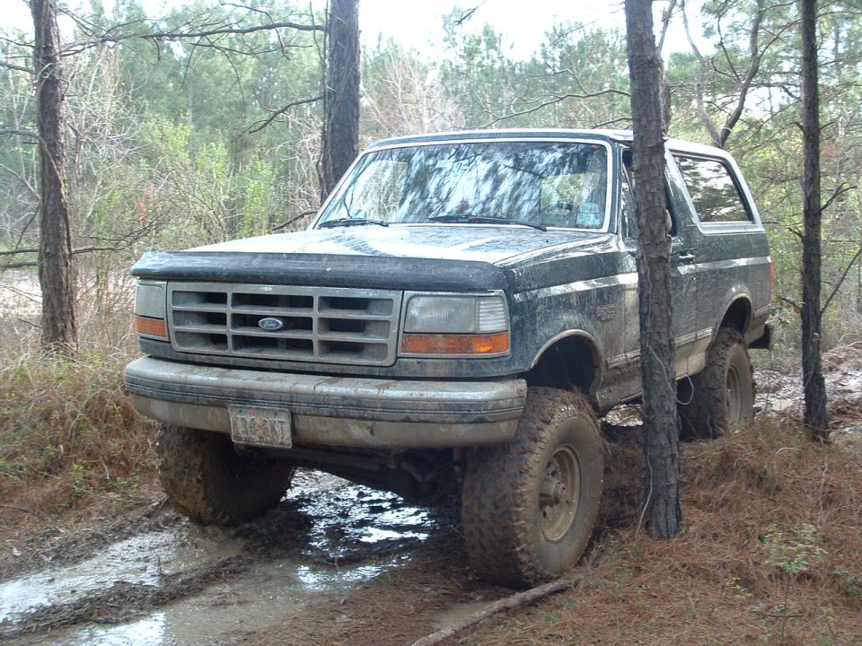 Dark green 1993 Ford Bronco with lifted suspension driving through mud