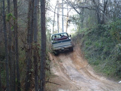 1993 Ford Bronco - Pickup truck navigates a steep, muddy off-road trail surrounded by trees.