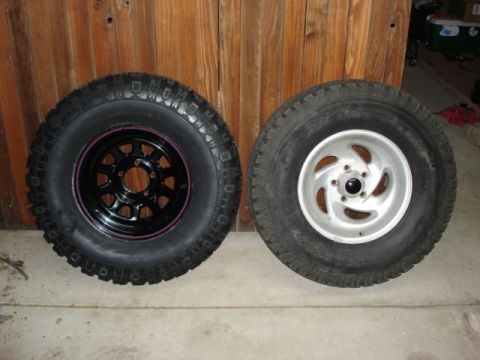 1987 Ford Bronco - A black-spoked wheel with a knobby tire sits next to a silver five-spoke wheel with a street tire.
