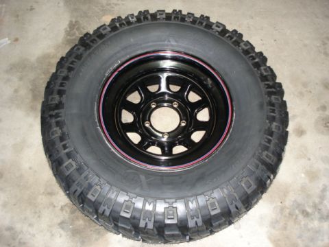 1987 Ford Bronco - A close-up view of a single off-road tire mounted on a black wheel with a red pinstripe.