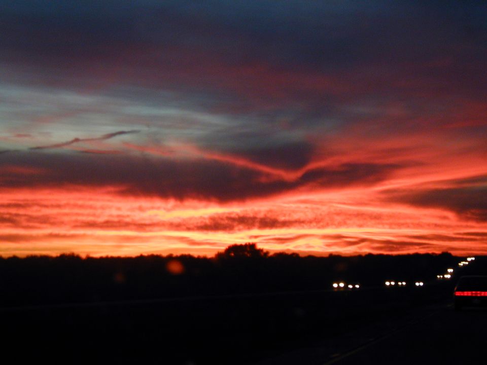 Vivid red sunset over a highway at dusk with distant headlights