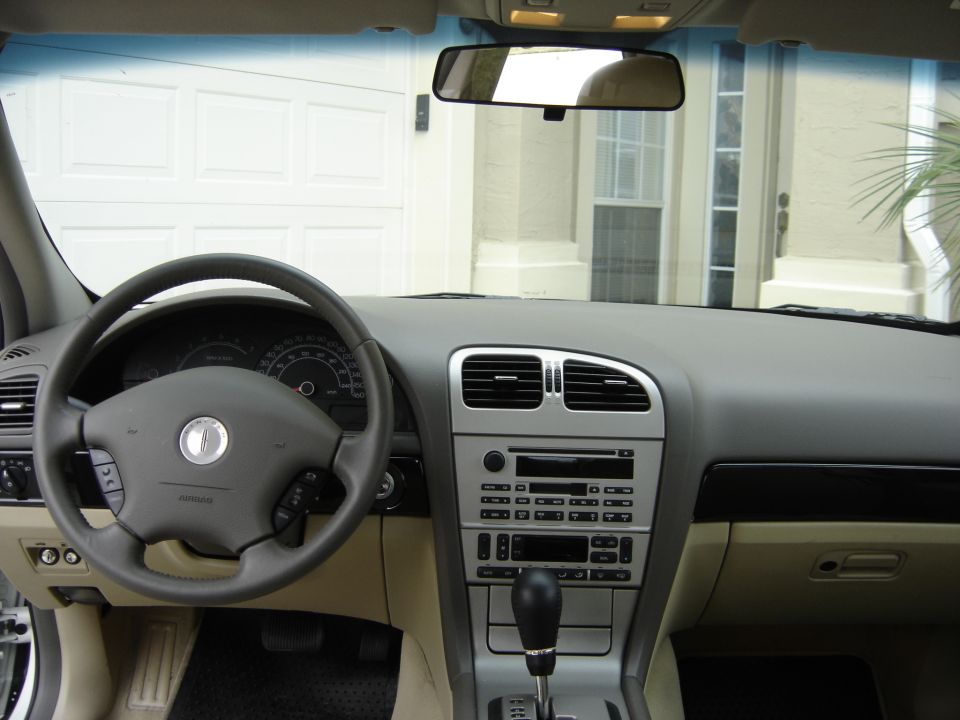 Car interior showing steering wheel, dashboard, and center console. Garage door visible through windshield