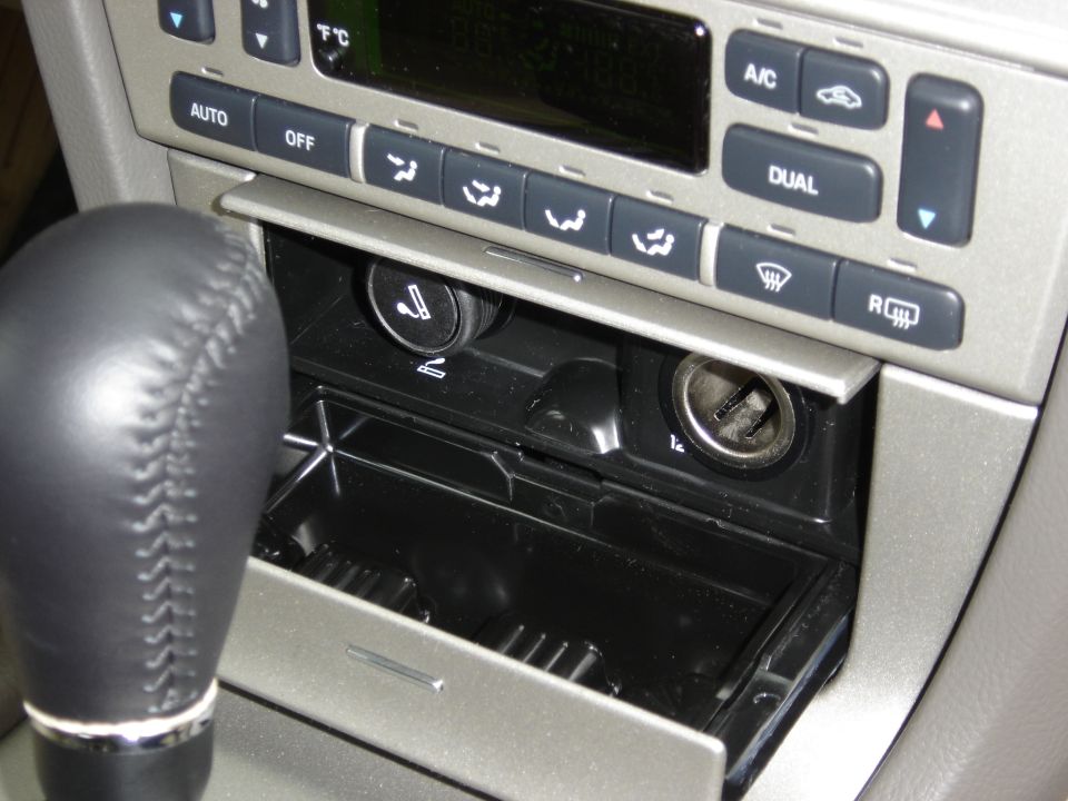 Car interior showing gear shift, climate controls, cigarette lighter, and open ashtray
