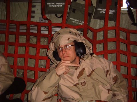 1988 Ford Bronco - A person in desert camouflage attire with headphones sits inside a cargo net, appearing to be in an aircraft.