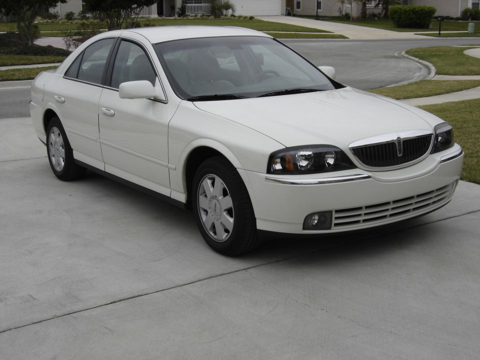 White sedan parked on a driveway, front 3/4 view. The grille and headlights are visible