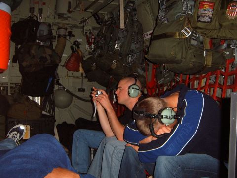 1988 Ford Bronco - People with headphones sit inside a transport aircraft, surrounded by parachute packs and equipment.