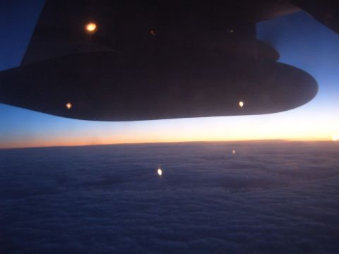 1988 Ford Bronco - View from an airplane window shows the wing and lights against a sunrise over a cloud layer.