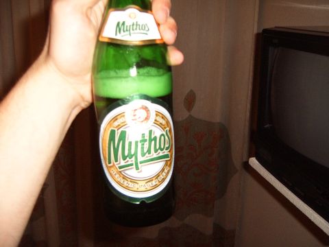 1988 Ford Bronco - A hand holds a bottle of Mythos beer in front of curtains and a television.