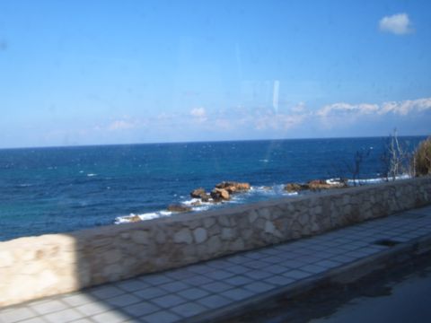 1988 Ford Bronco - A scenic view of the ocean with waves crashing on rocks, bordered by a stone wall and tiled walkway.