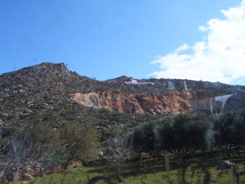 1988 Ford Bronco - A view of a rocky hillside with sparse vegetation and a building structure visible on the ridge under a blue sky.