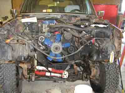 1988 Ford Bronco - The engine bay of a vehicle is shown with a prominent blue fan and various hoses and components. The front tires are visible.