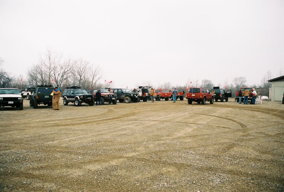 Several SUVs parked in a gravel lot with people standing around