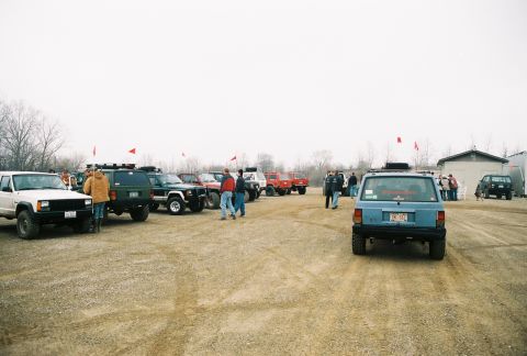 1995 Ford Bronco - A gathering of SUVs and trucks on a gravel lot under an overcast sky.