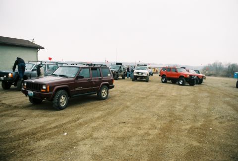 1995 Ford Bronco - A group of Jeep Cherokees are gathered on a dirt lot under an overcast sky.