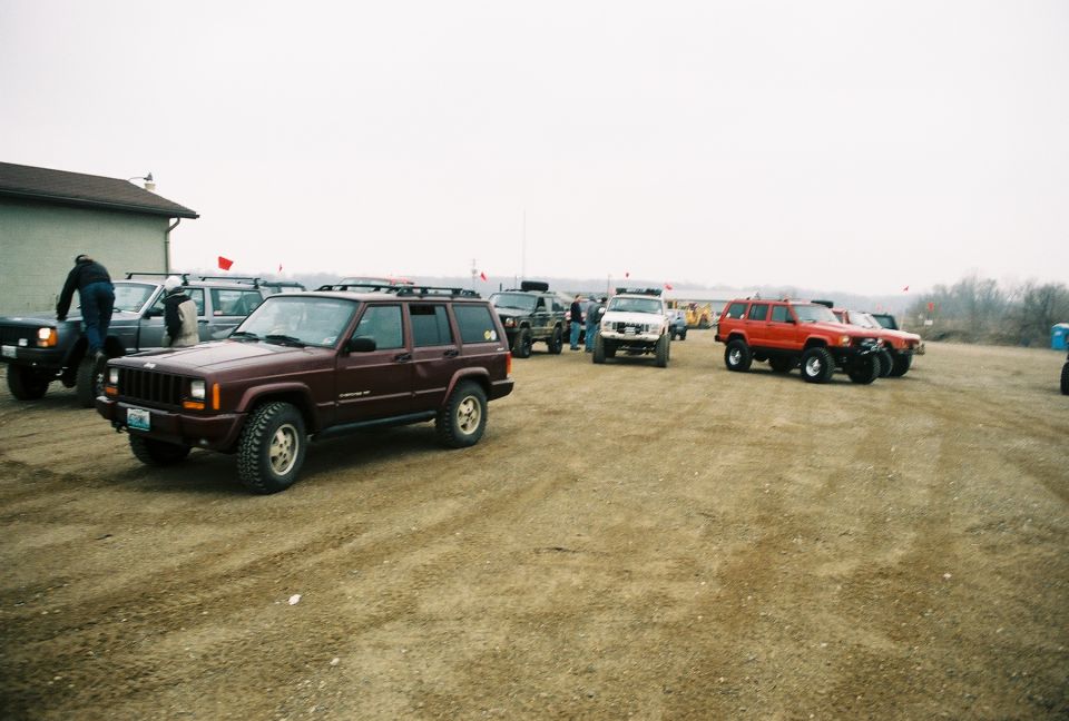 Several Jeep Cherokees parked on a dirt lot. One maroon Cherokee is in the foreground
