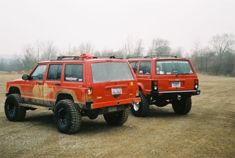 1995 Ford Bronco - Two red Jeep Cherokees are parked in an outdoor area with trees in the background.