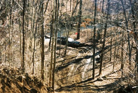 1995 Ford Bronco - A 1995 Ford Bronco navigates a muddy, wooded trail during an off-road excursion.