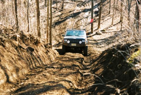 1995 Ford Bronco - Jeep Cherokee XJ navigates a challenging off-road trail through a forest.