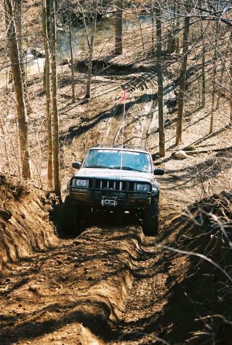 1995 Ford Bronco - Jeep Cherokee XJ navigates a challenging off-road trail through a wooded area.